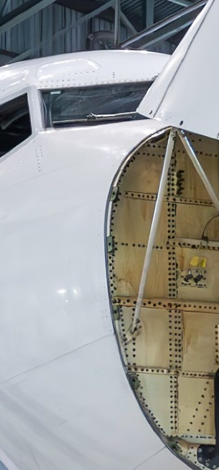 Front view of the white passenger airliner under maintenance in the aircraft hangar. The plane has opened weather radar. Checking mechanical systems for flight operations