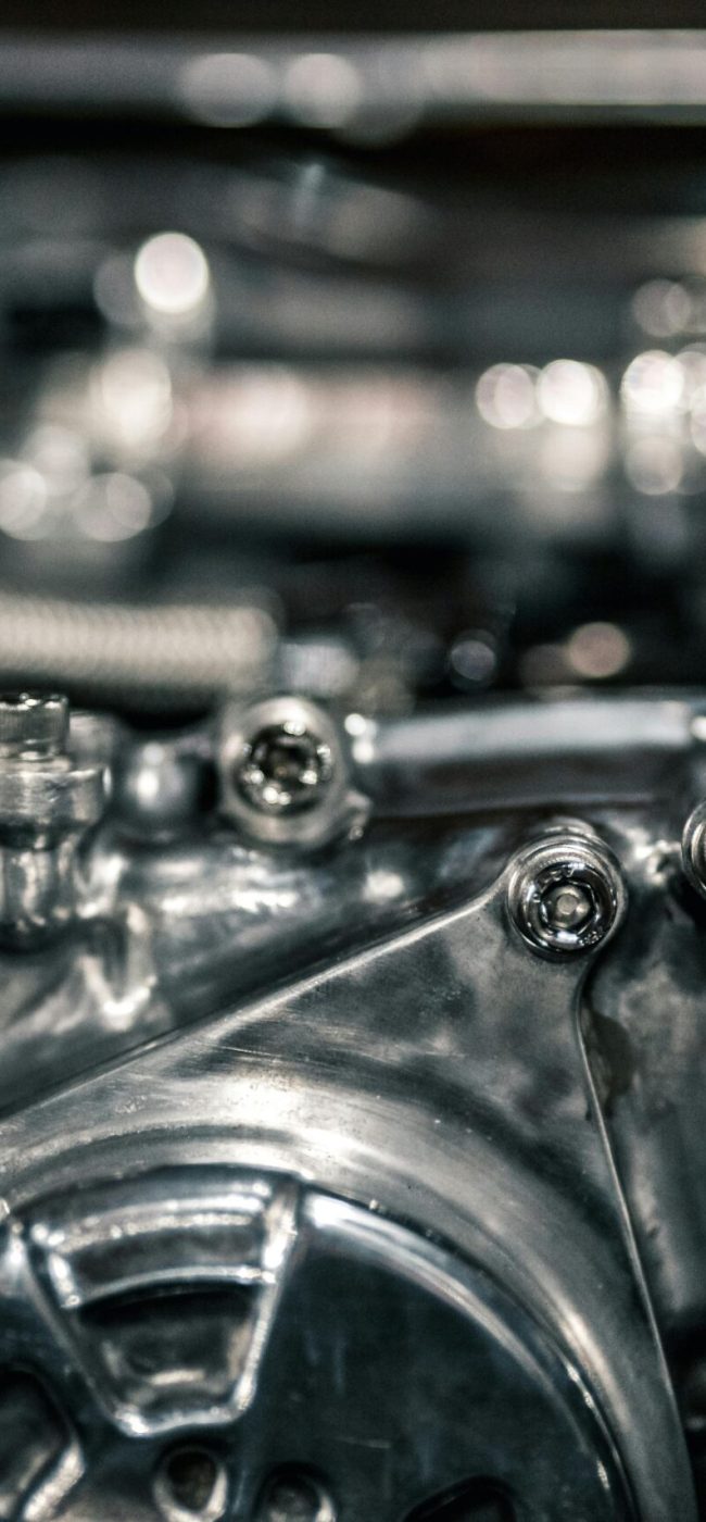 Macro shot of a polished metallic engine component with secure bolts and tension pulleys in a high-precision machine setup