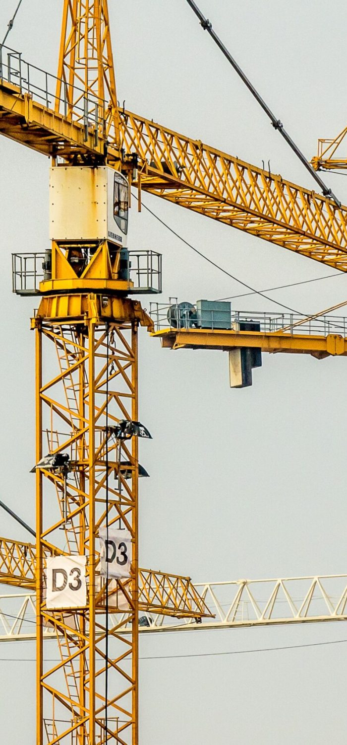 Yellow tower construction cranes operating on a construction site with lattice booms and masts against a gray sky